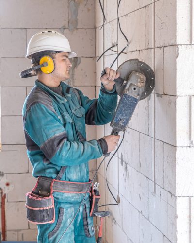 An electrician construction worker in a protective helmet at a work facility works with a grinder.