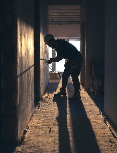 A construction electrician cuts a voltage cable during a repair, silhouette in the light of the setting sun.